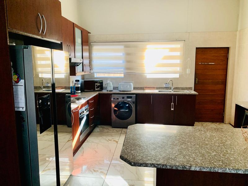 Modern kitchen featuring dark wood cabinetry, granite countertops, integrated appliances, and polished tiled flooring with ample natural light.