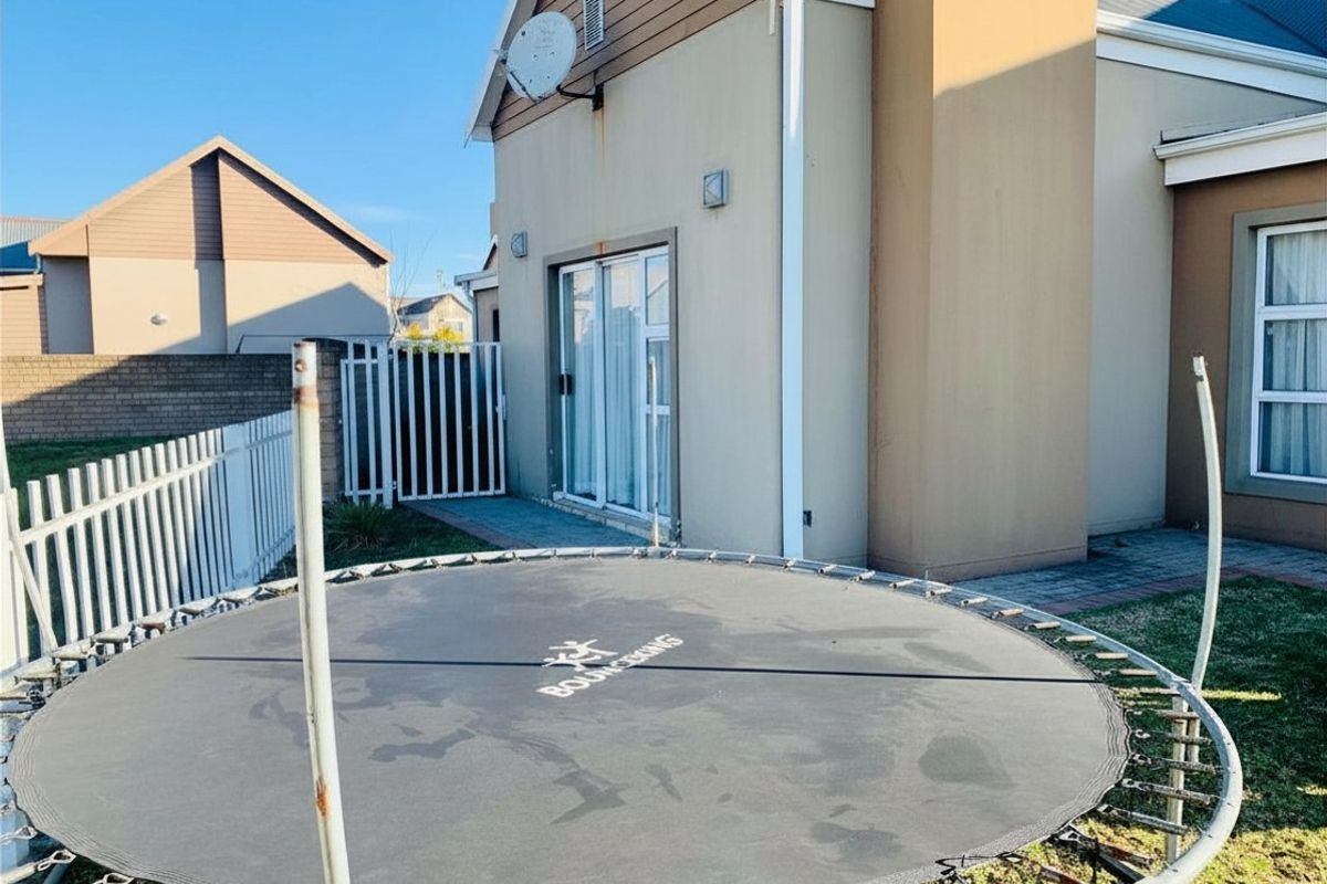 Rear exterior view of the property featuring a paved walkway, sliding glass door access, and perimeter fencing.