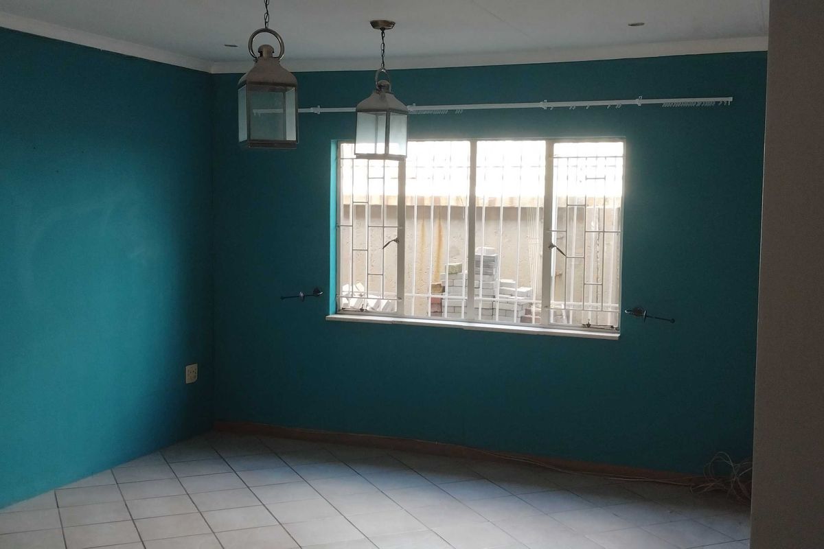 An empty living room featuring tiled flooring, teal-painted walls, and security bars on the window.