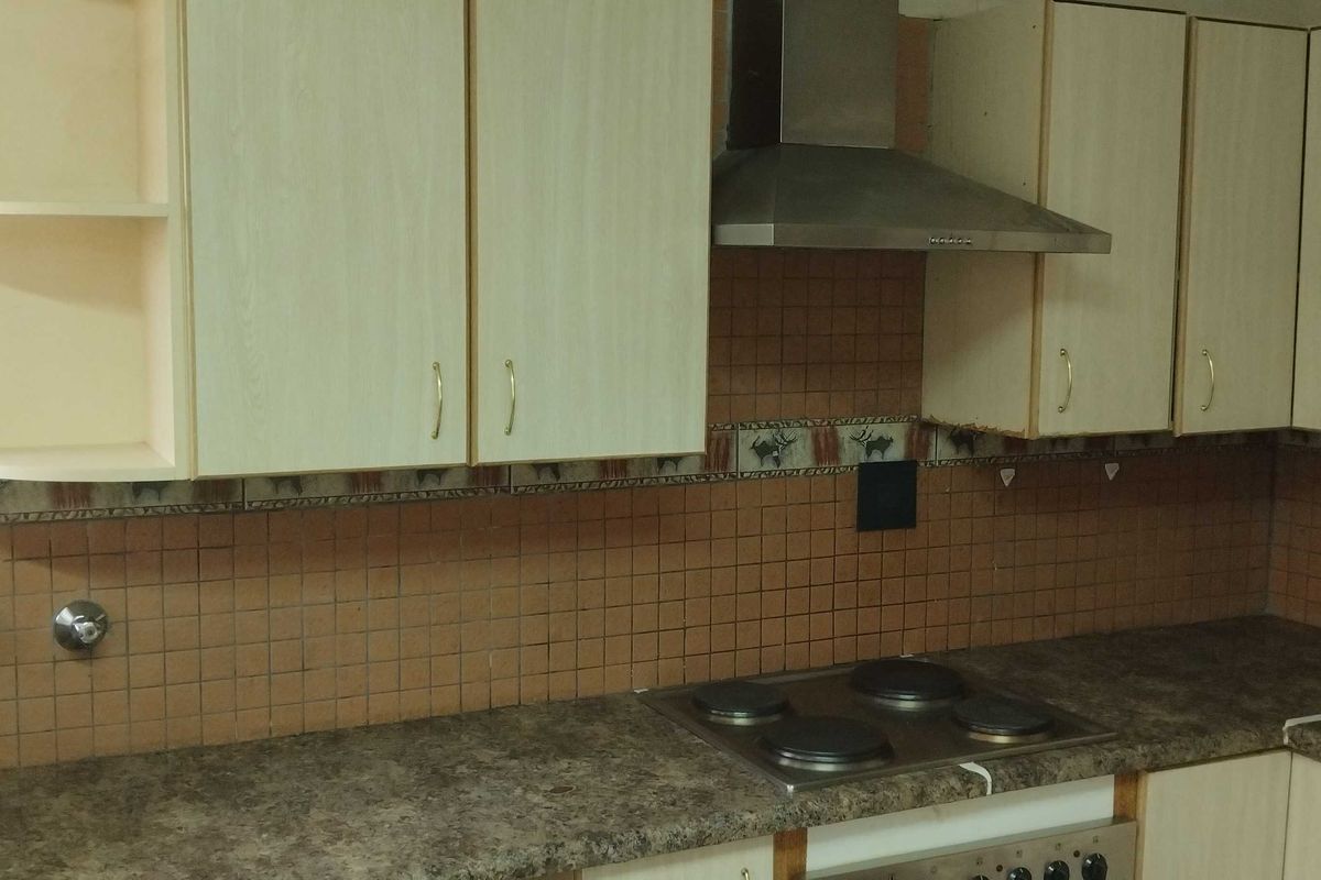 A functional kitchen featuring laminate cabinetry, a built-in electric hob, extractor fan, and tiled backsplash with neutral countertops.