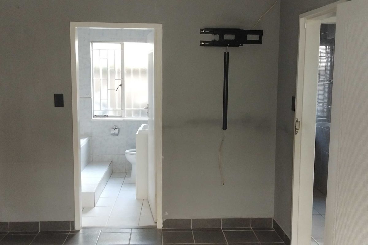 An empty bedroom featuring tiled flooring, a wall-mounted TV bracket, and direct access to an en-suite bathroom.