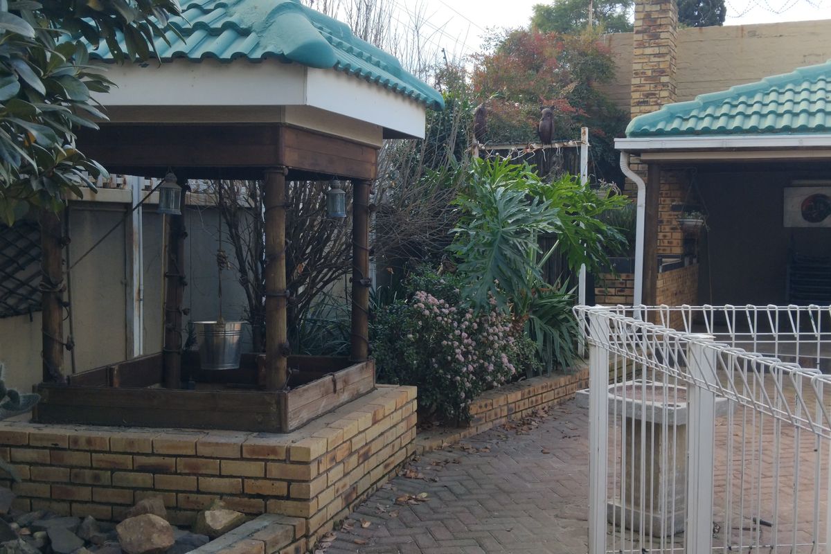Rear garden area featuring brick paving, a covered patio space, and a decorative wishing well structure set against a brick boundary wall.