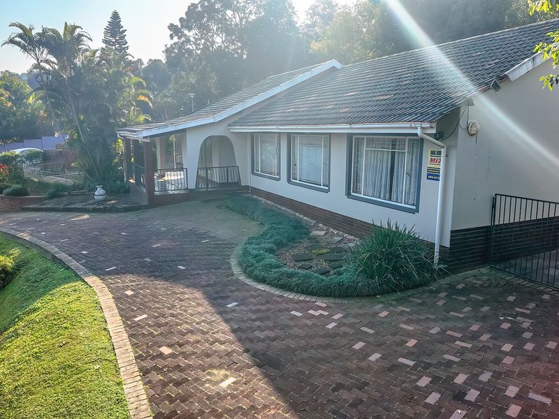 Front elevation of a residential house featuring a tiled roof, covered entrance, and a spacious brick-paved driveway set within a landscaped garden.