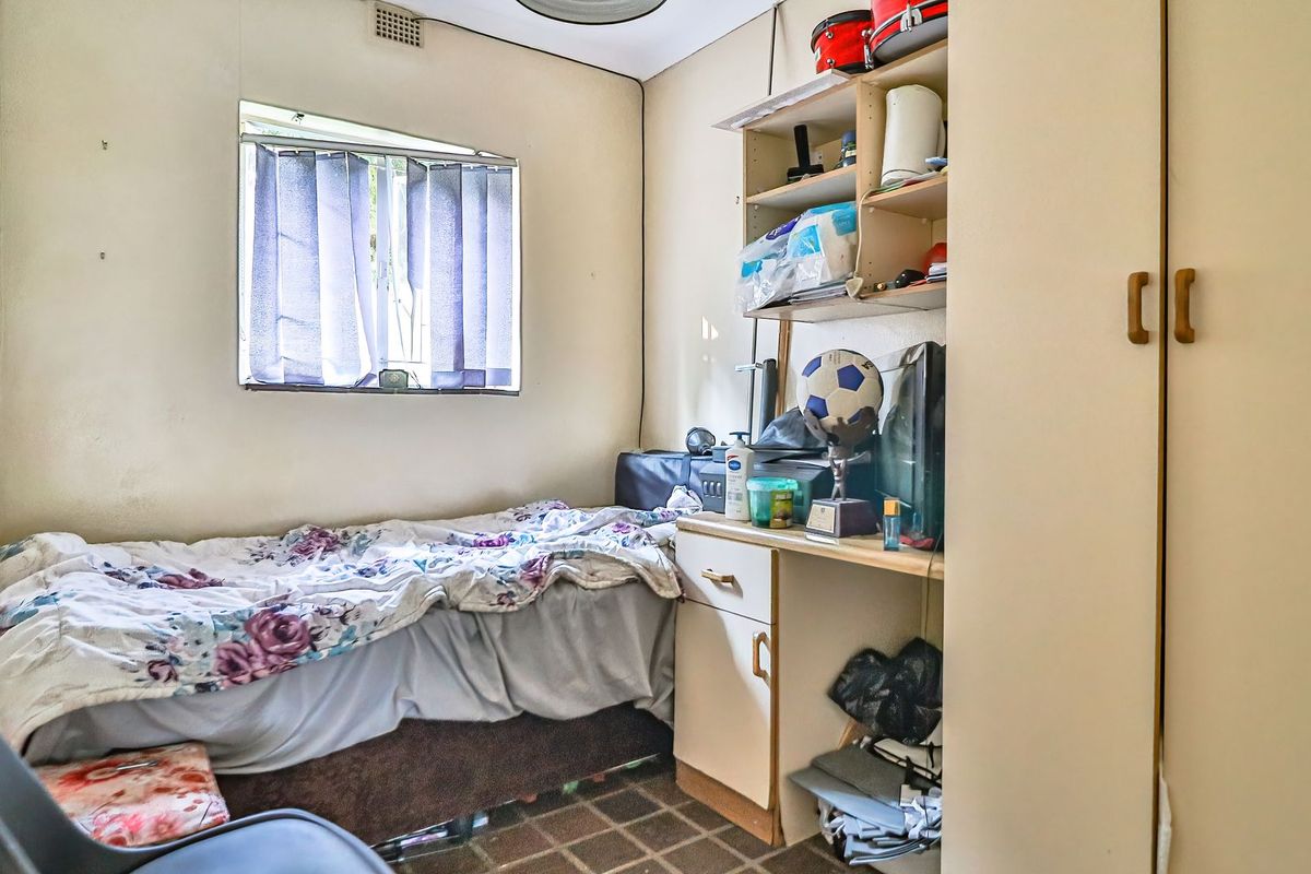 A compact bedroom featuring built-in cabinetry, including a wardrobe, desk, and shelving unit, with a window providing natural light.