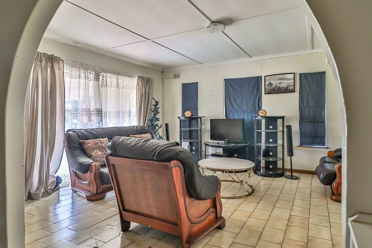 A living room featuring tiled flooring and an arched entryway, offering a functional space with potential for cosmetic updates.
