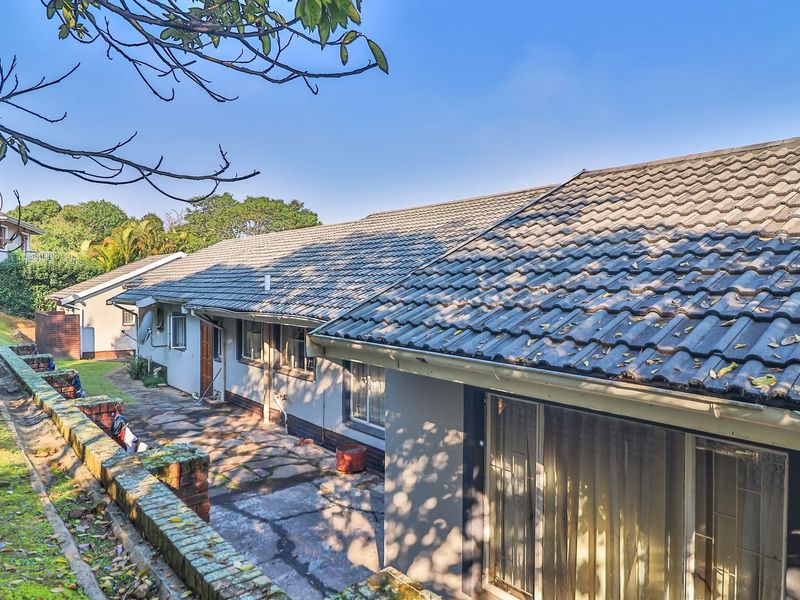 Rear exterior view of the house featuring a paved patio area, brick retaining wall, and concrete tiled roof.