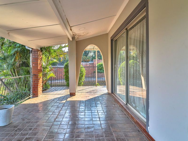 A covered patio area featuring tiled flooring, brick support pillars, and an arched architectural detail, providing access to the interior through sliding glass doors.