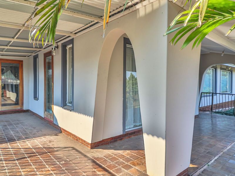 A spacious covered patio featuring arched masonry columns, tiled flooring, and timber-framed glass doors, offering a versatile outdoor living area.