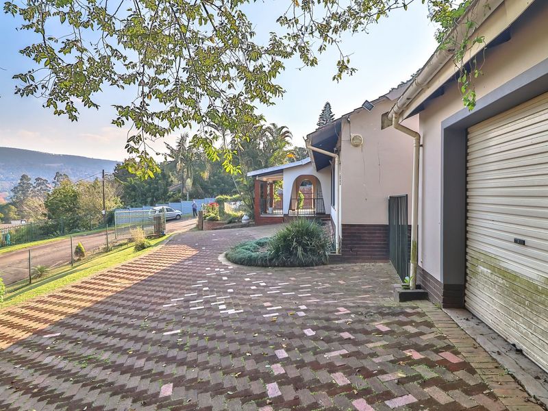 Front exterior view featuring a paved driveway, roller garage door, and covered patio area with surrounding garden and mountain views.