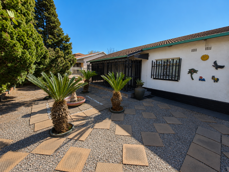 A well-maintained rear exterior area featuring a paved patio, gravel landscaping, and security bars on the windows.