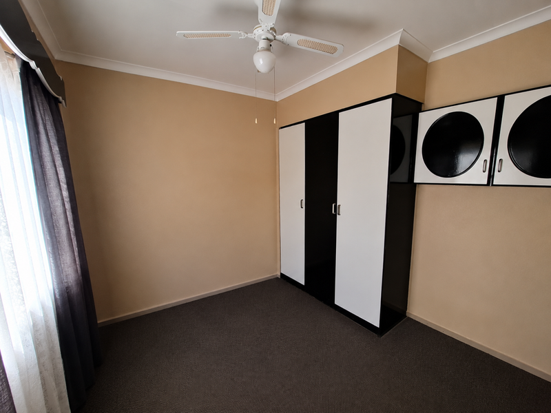 A clean, empty bedroom featuring neutral walls, dark carpet flooring, a ceiling fan, and built-in storage cabinetry.
