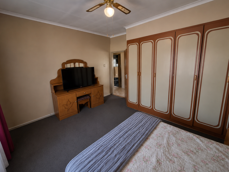 A bedroom featuring built-in cupboards, a ceiling fan, and neutral wall finishes, with an adjoining en-suite bathroom visible through the doorway.
