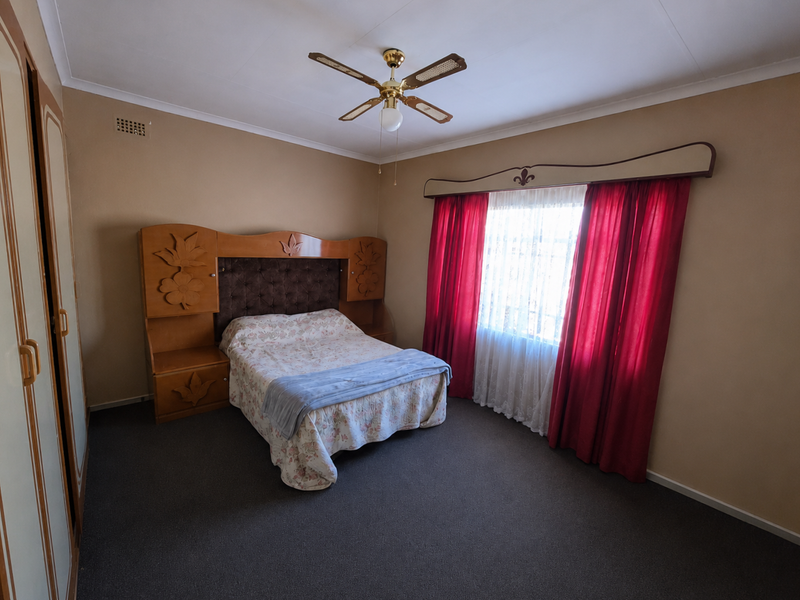 A spacious bedroom featuring built-in cupboards, a ceiling fan, and neutral wall tones, offering a functional layout ready for modern updates.