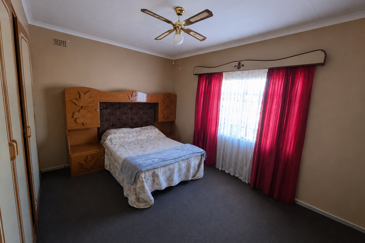 A spacious bedroom featuring built-in cupboards, a ceiling fan, and neutral wall tones, offering a functional layout ready for modern updates.