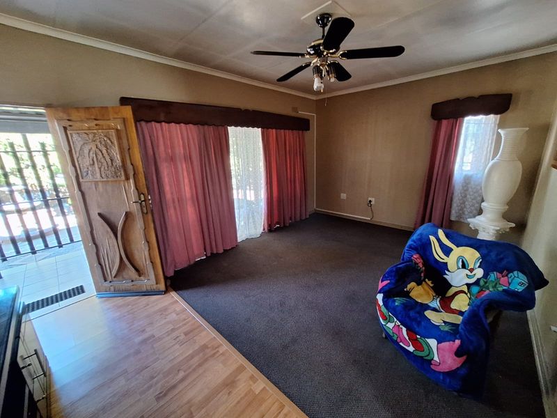 A living room featuring a ceiling fan, carpeted flooring, and a decorative wooden entrance door, offering a functional space with potential for modernization.