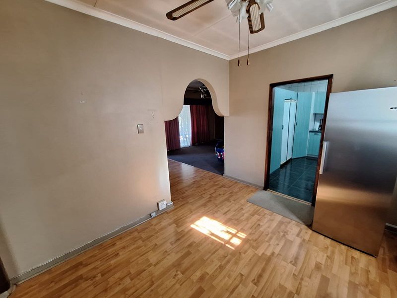 An open-plan living area featuring laminate flooring, a ceiling fan, and a distinctive arched doorway leading to an adjacent room.