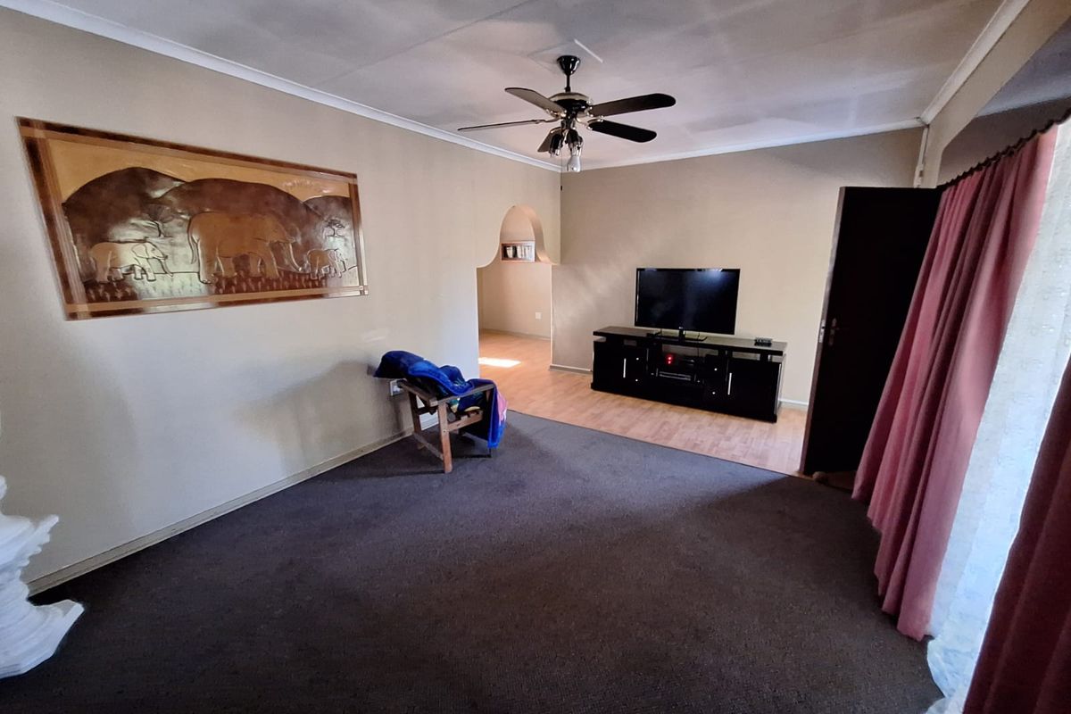 Spacious living room featuring a ceiling fan, neutral wall tones, and a mix of carpet and laminate flooring with an arched transition to adjacent space.