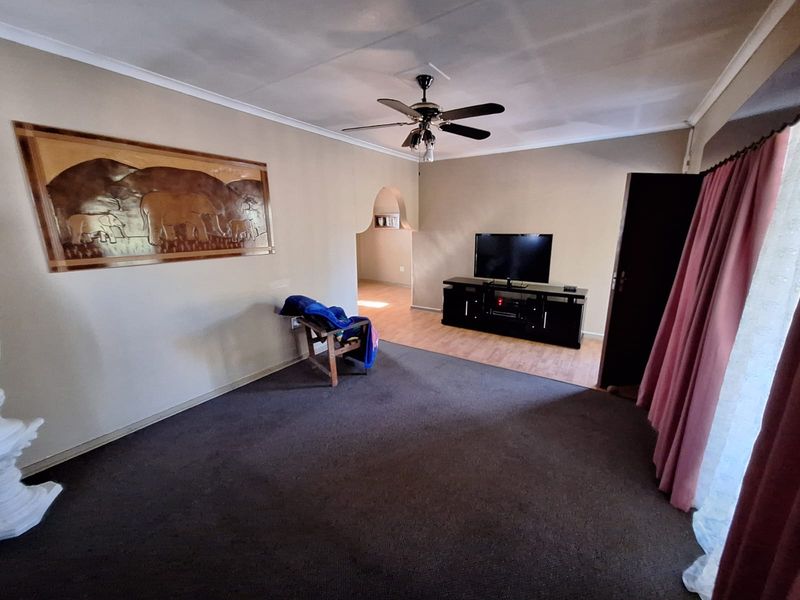 Spacious living room featuring a ceiling fan, neutral wall tones, and a mix of carpet and laminate flooring with an arched transition to adjacent space.