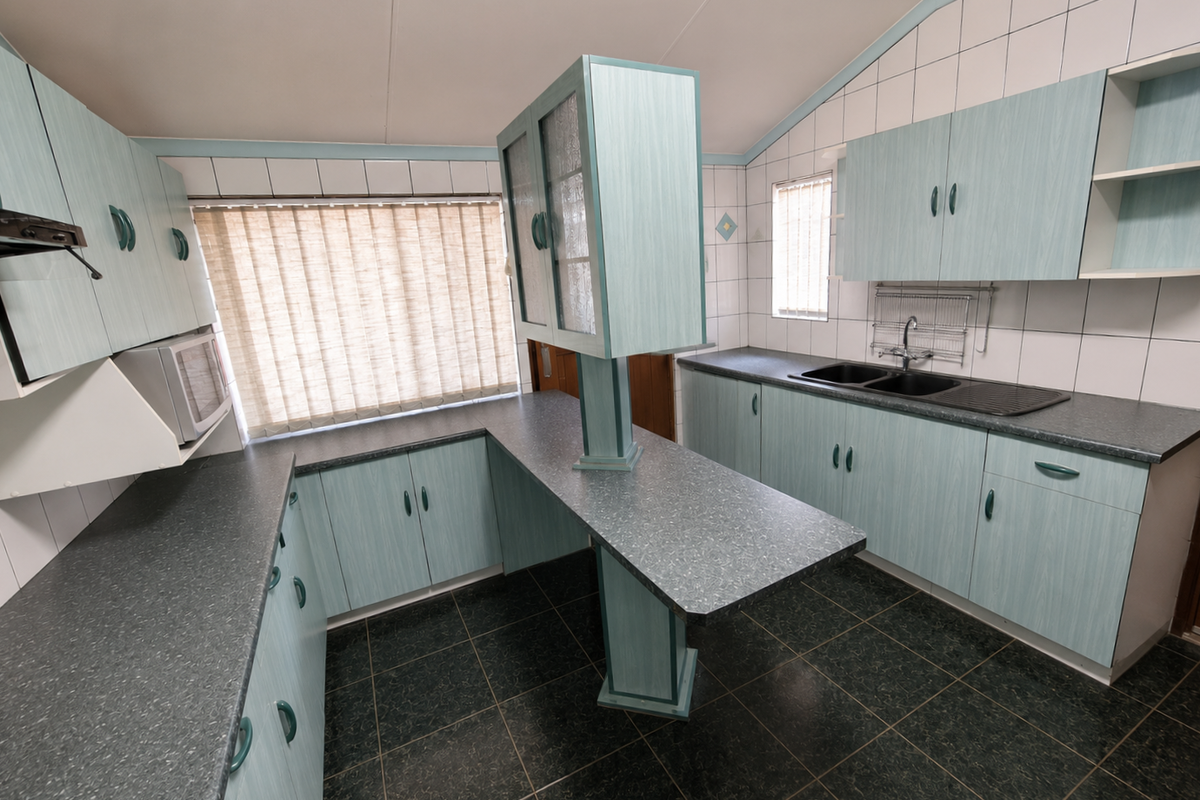 A functional kitchen featuring light blue laminate cabinetry, dark countertops, a double basin sink, and tiled backsplash with ample storage space.