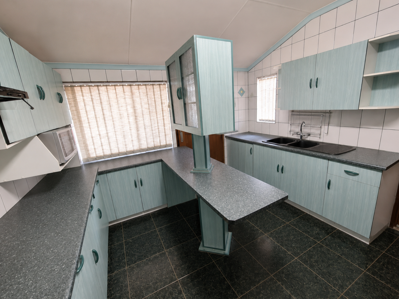 A functional kitchen featuring light blue laminate cabinetry, dark countertops, a double basin sink, and tiled backsplash with ample storage space.