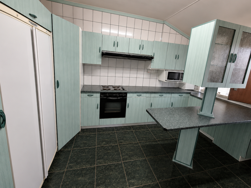 A functional kitchen featuring light green cabinetry, dark laminate countertops, a built-in oven and hob, and tiled flooring throughout.