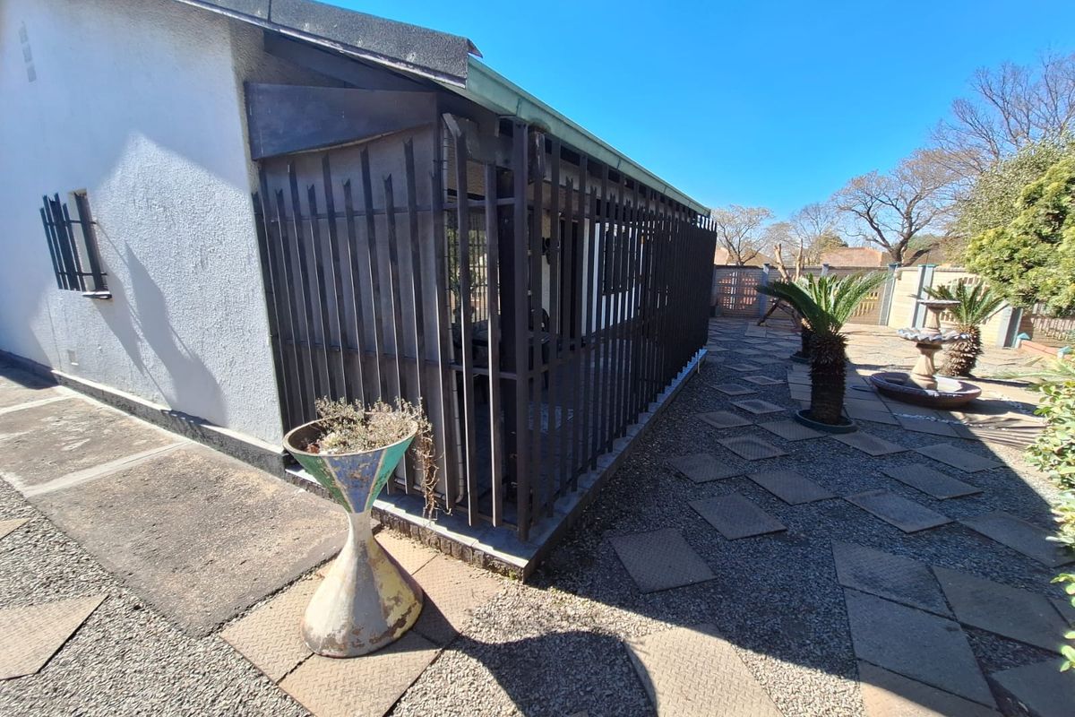 Rear exterior view featuring a paved patio area, stone fountain, and security-fenced enclosure attached to the main dwelling structure.