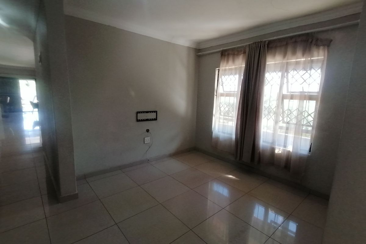 A bright, empty living room featuring neutral tiled flooring, large windows with security bars, and wall-mounted electrical points.