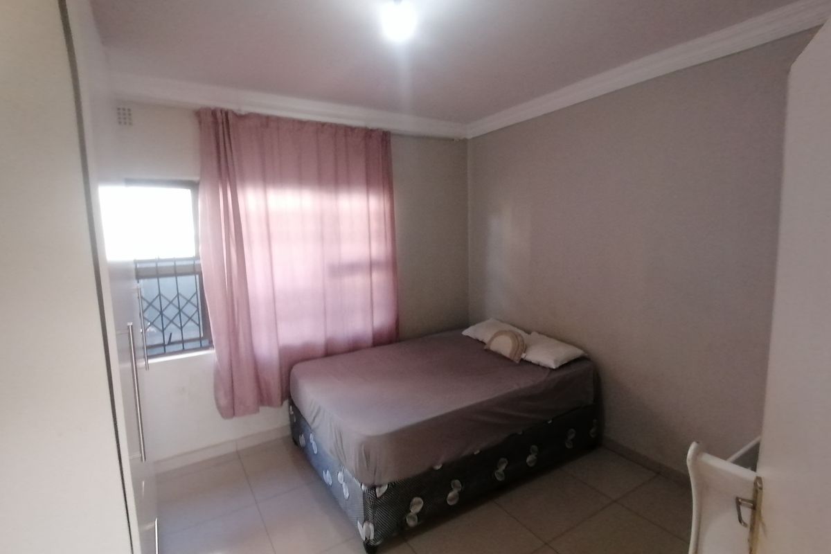 A functional bedroom featuring tiled flooring, built-in cupboard space, and a window with security bars.