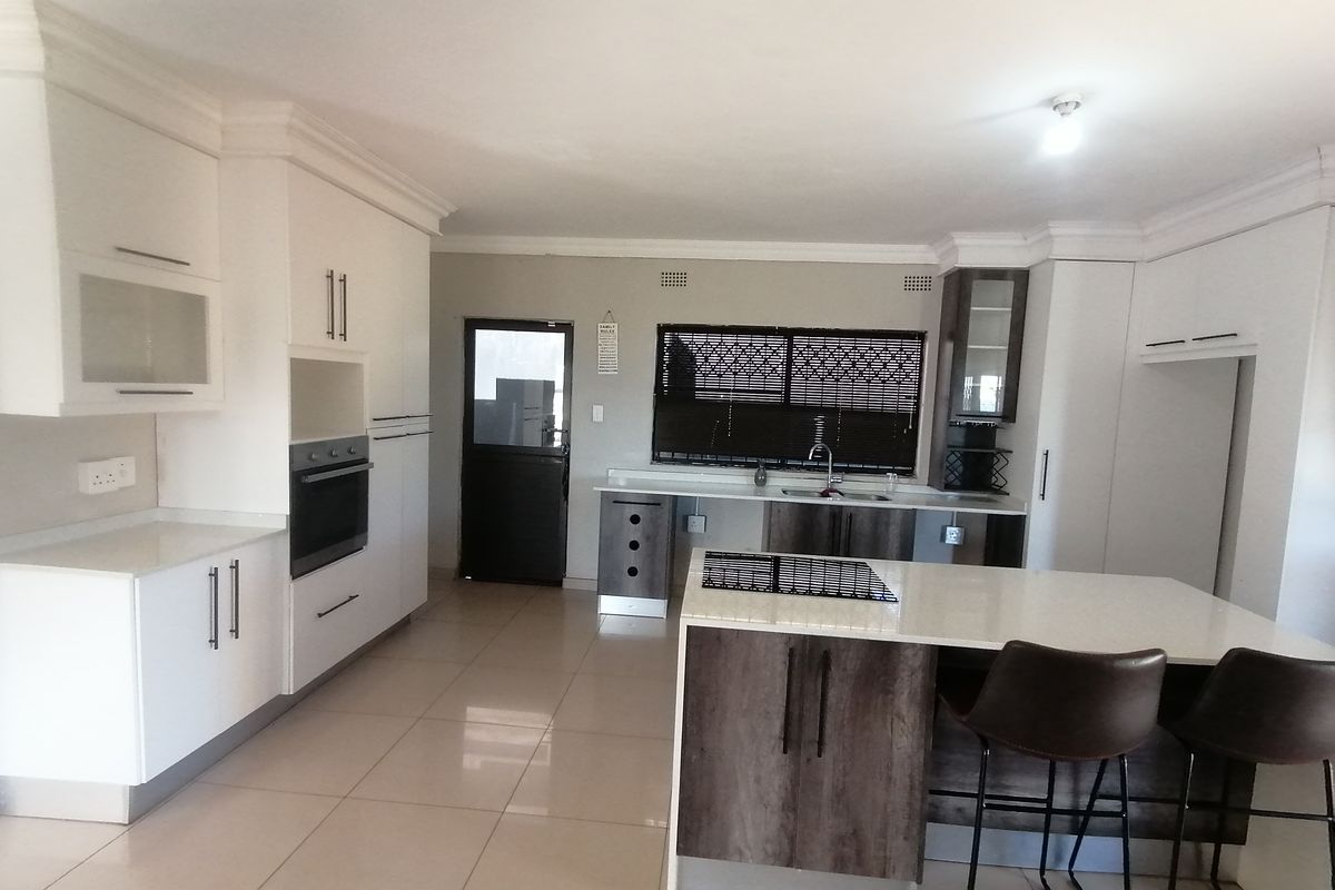 Modern kitchen featuring white cabinetry, contrasting wood-tone island, stone countertops, built-in oven, and ceramic cooktop with tiled flooring throughout.