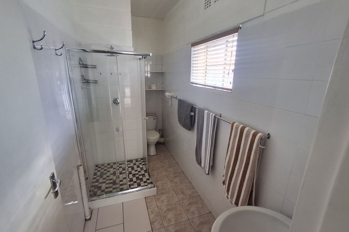 A functional bathroom featuring a glass-enclosed shower, toilet, and wall-mounted fixtures with neutral tiling throughout.