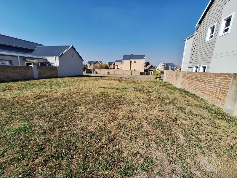 A vacant residential plot featuring a grass lawn enclosed by brick boundary walls, situated within a developed suburban neighborhood.