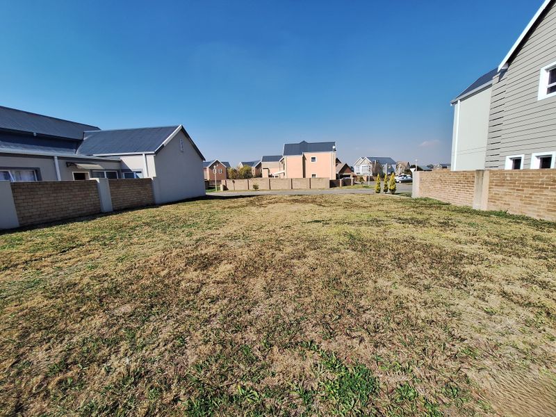 A vacant residential plot featuring a grass lawn enclosed by brick boundary walls, situated within a developed suburban estate.