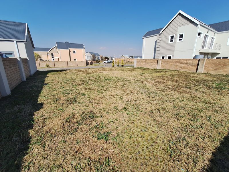 A vacant residential plot featuring a grass lawn enclosed by brick boundary walls within a developed estate setting.