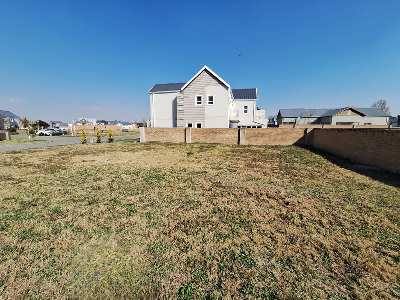 A vacant residential plot featuring a level grass surface and a perimeter brick boundary wall in a suburban estate setting.