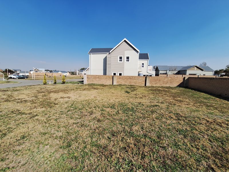 A vacant residential plot featuring a level grass lawn and a perimeter brick boundary wall in a developed suburban estate.