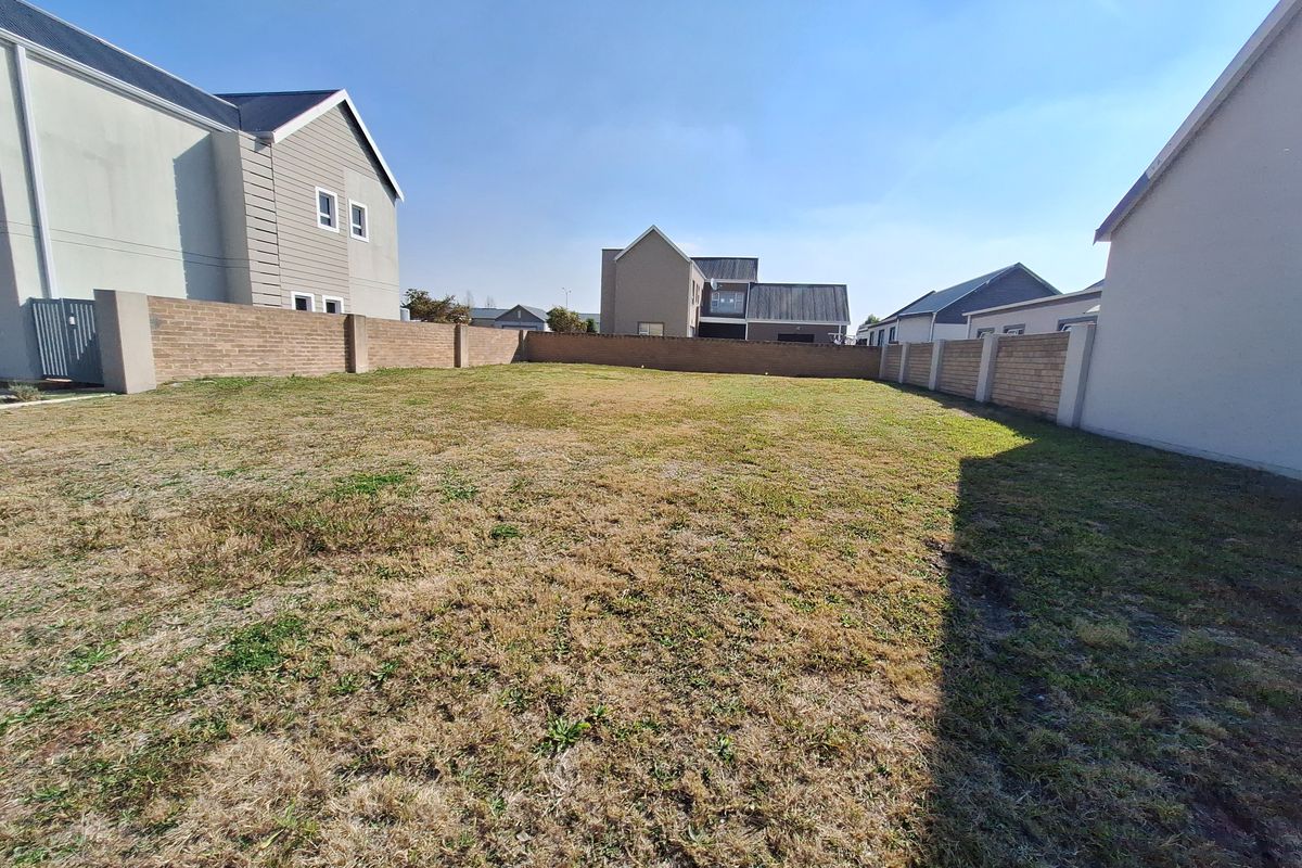 A vacant residential plot featuring a grass lawn and enclosed by brick boundary walls, situated within a developed residential estate.