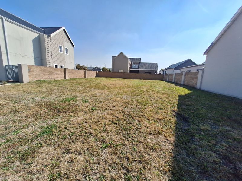 A vacant residential plot featuring a grass lawn and enclosed by brick boundary walls, situated within a developed residential estate.