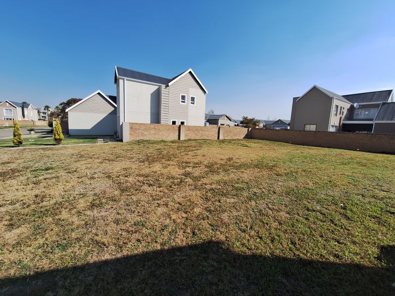 A spacious, level residential plot featuring a perimeter brick boundary wall and established lawn, situated within a developed residential estate.