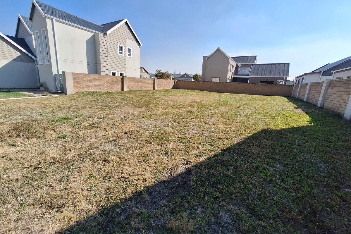 A vacant residential plot featuring a level grass lawn enclosed by perimeter brick boundary walls in a developed estate setting.