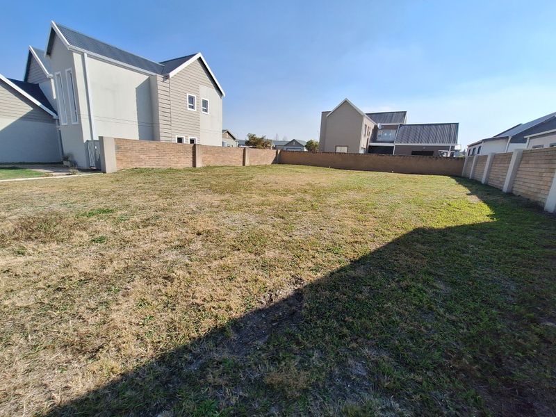 A vacant residential plot featuring a level grass lawn enclosed by perimeter brick boundary walls in a developed estate setting.