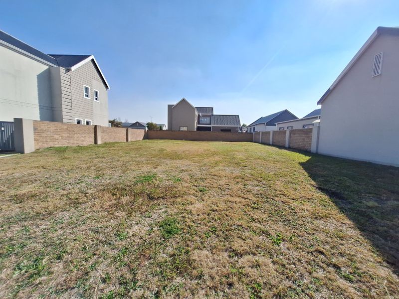 A vacant residential plot enclosed by perimeter brick walls, situated within a developed neighborhood setting.