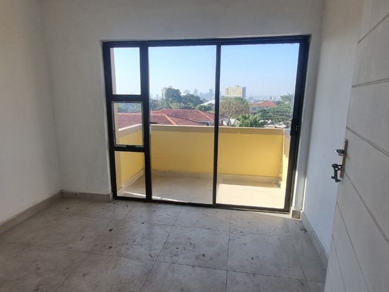 An empty bedroom featuring tiled flooring and a large sliding glass door that opens onto a private balcony with urban views.