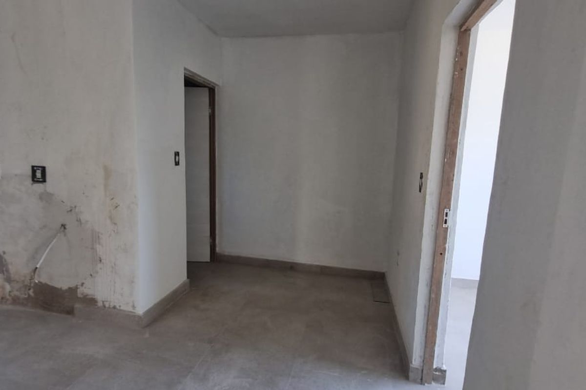 An empty, unfinished living area featuring tiled flooring and visible wall damage, presenting a blank canvas for renovation and interior design.