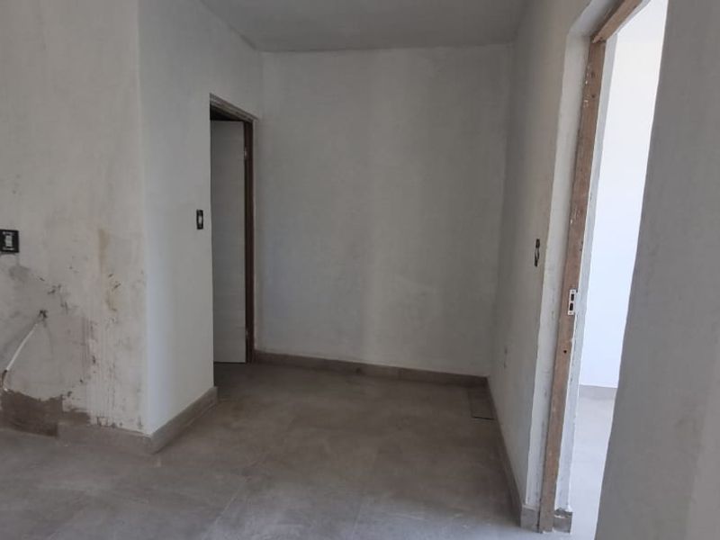 An empty, unfinished living area featuring tiled flooring and visible wall damage, presenting a blank canvas for renovation and interior design.