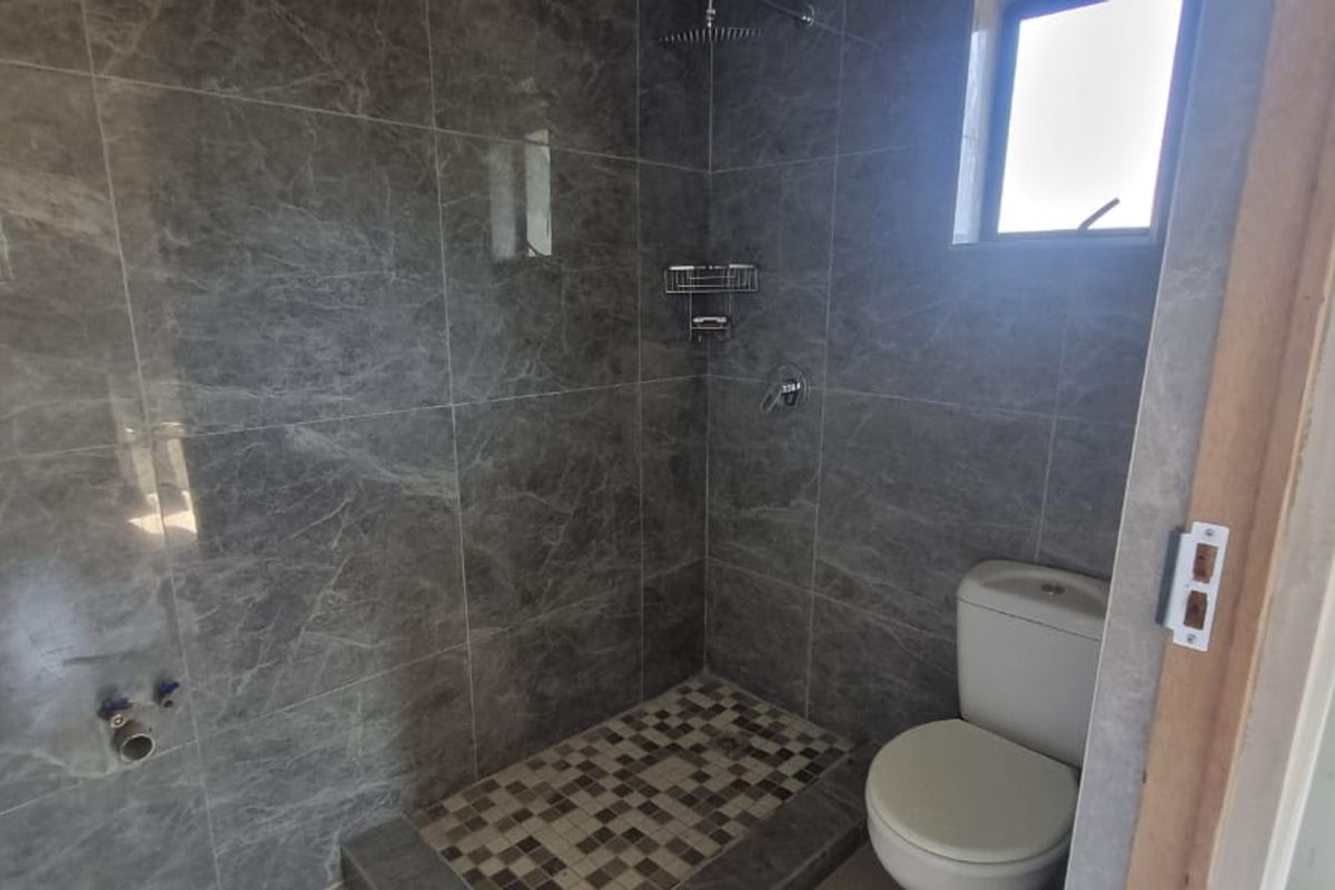 A modern bathroom featuring grey marble-look wall tiles, a walk-in shower with a rain shower head, mosaic floor tiling, and a standard toilet.