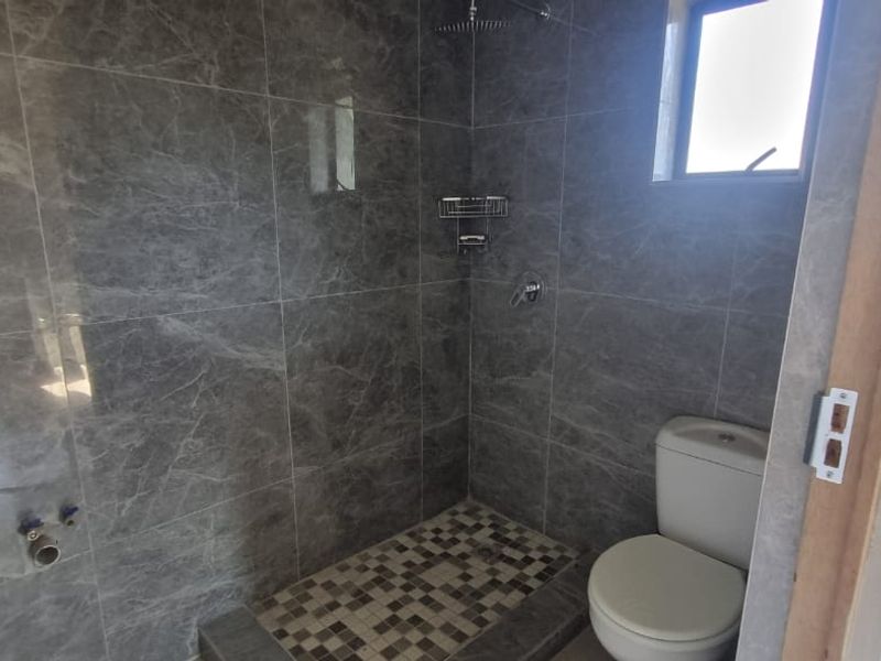 A modern bathroom featuring grey marble-look wall tiles, a walk-in shower with a rain shower head, mosaic floor tiling, and a standard toilet.