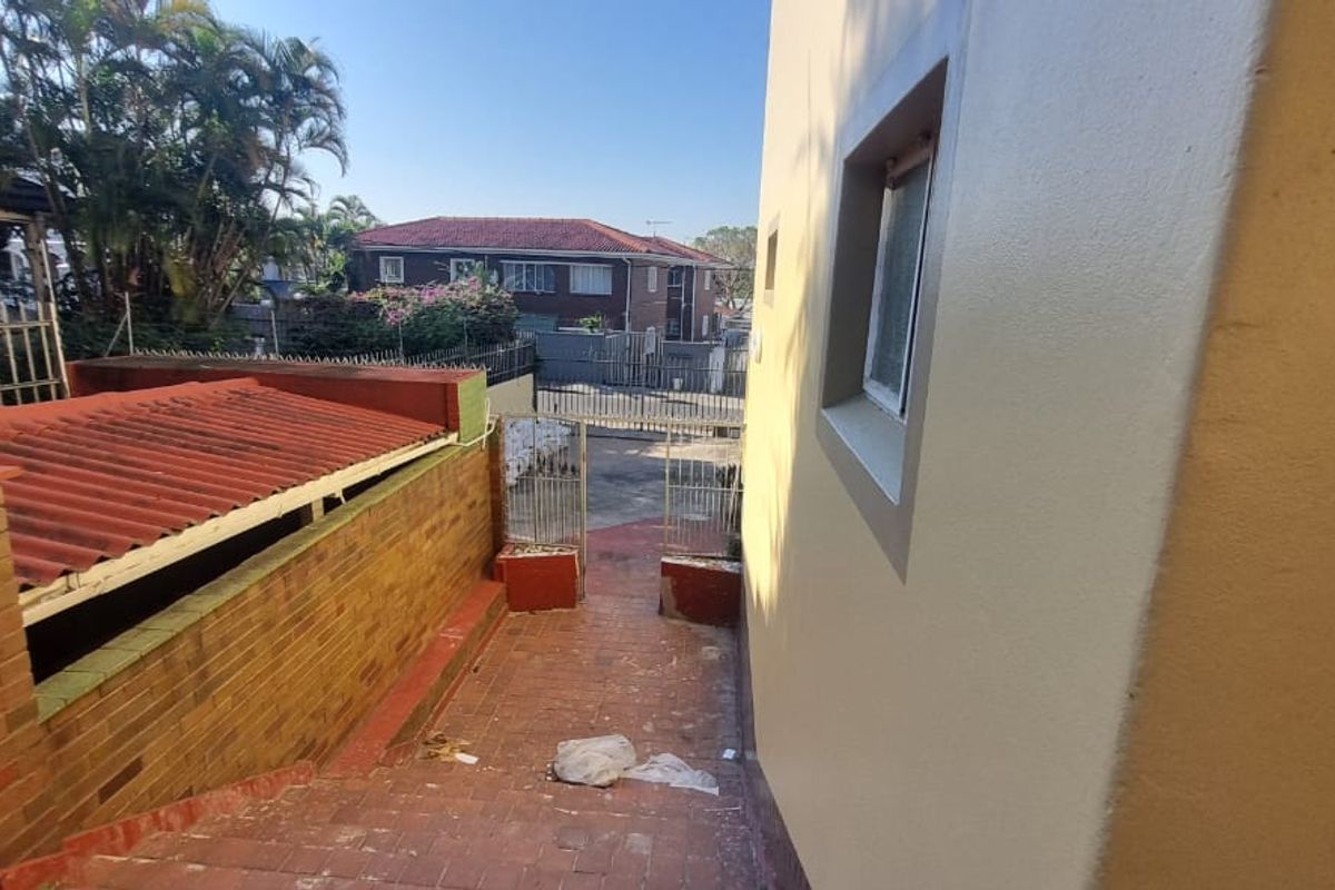 A view of the exterior rear walkway featuring a brick boundary wall, tiled roof section, and metal security gate access.