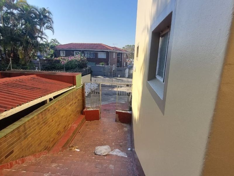 A view of the exterior rear walkway featuring a brick boundary wall, tiled roof section, and metal security gate access.