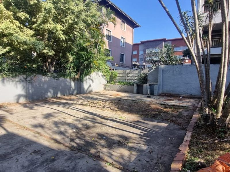 A spacious rear outdoor area featuring concrete paving, a perimeter boundary wall, and a built-in braai, offering potential for landscaping and renovation.