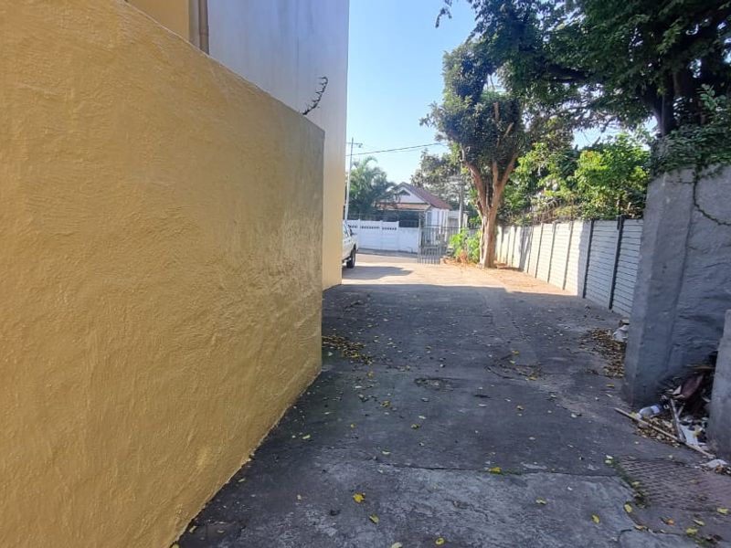 A view of the rear exterior driveway area featuring concrete paving and boundary walls with visible signs of wear and maintenance requirements.